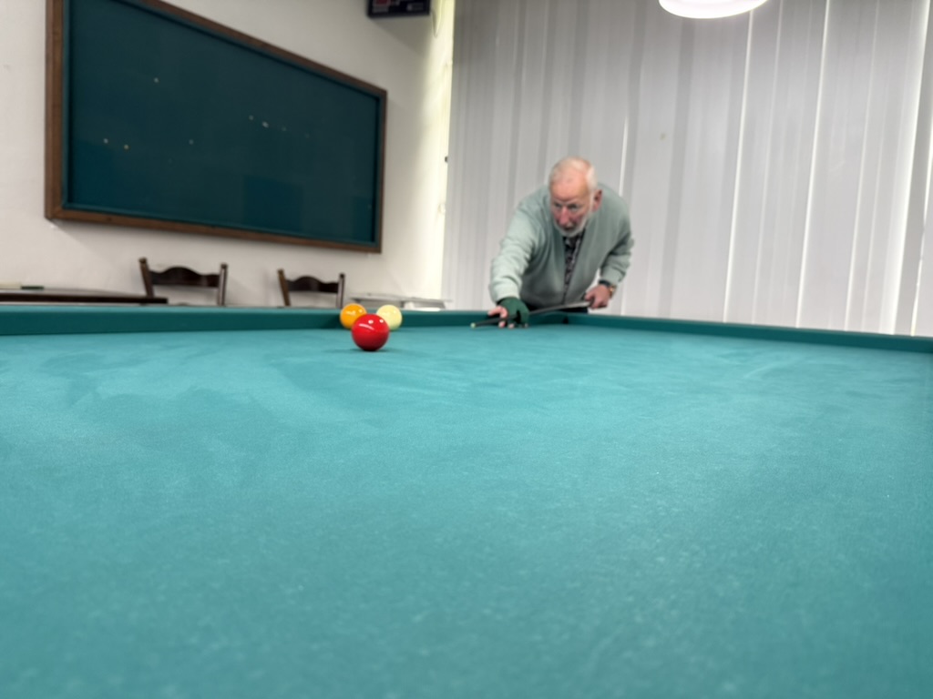 Ko speelt een stoot aan de biljarttafel, gezien vanaf het laken met de rode bal op de voorgrond